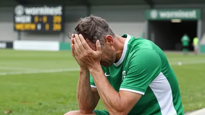 A 50-year-old, 5'10" Werderaner midfielder in a plain green and white polyester training top, his face set in a mix of...
