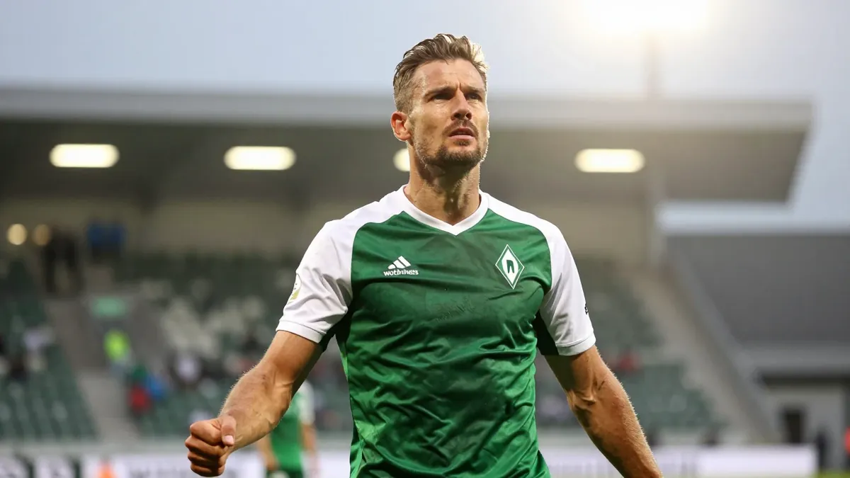 A 35-year-old Werderaner striker with a rugged build, his face set in intense focus, takes a moment to celebrate after...